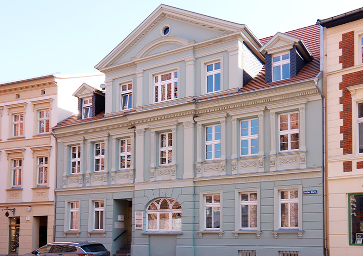 Der Standort in Perleberg. Ein zetral gelegenes Anwesen mit hellblauer Fassade und weißen Stuck-Verzierungen.